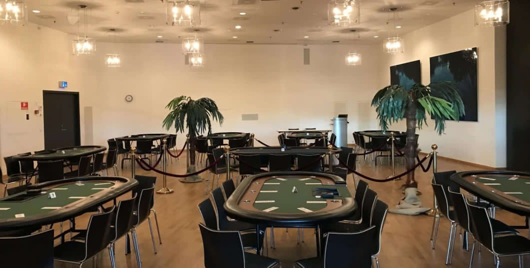 Pokerlokale med borde, palmer og velourreb klar til turnering
